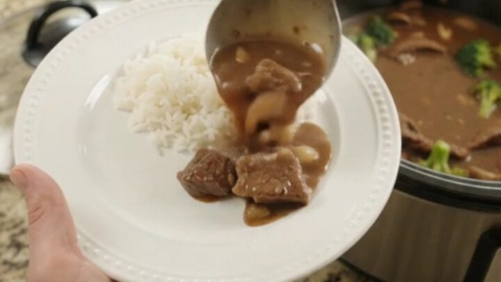 Slow cooker full of tender flank steak, broccoli, and mushrooms in glossy bourbon gravy
