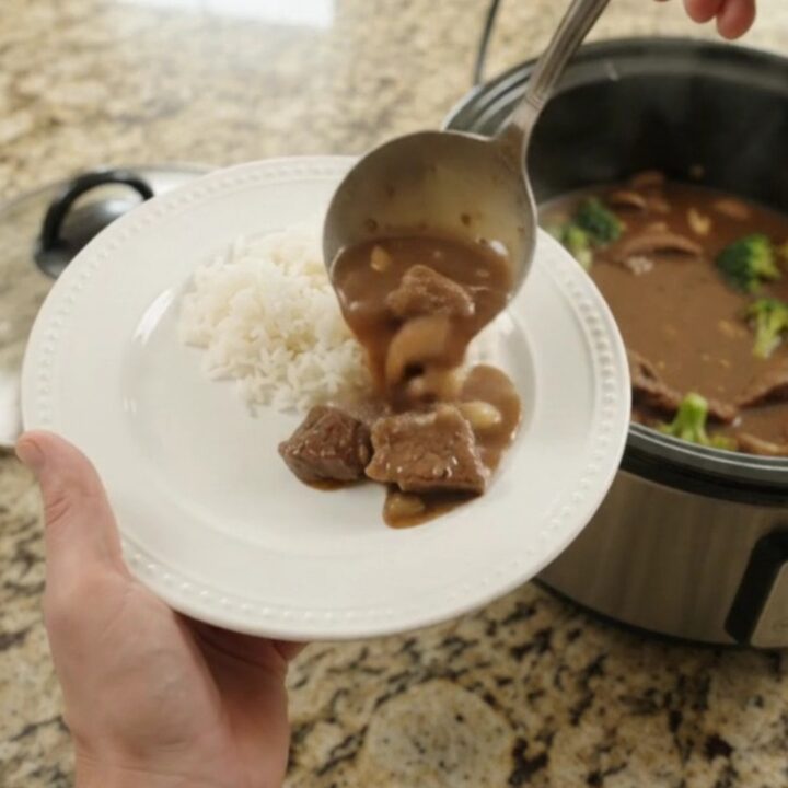 Slow cooker full of tender flank steak, broccoli, and mushrooms in glossy bourbon gravy