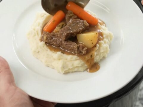 Slow cooker filled with tender flank steak, baby carrots, and red potatoes in a golden butter au jus.