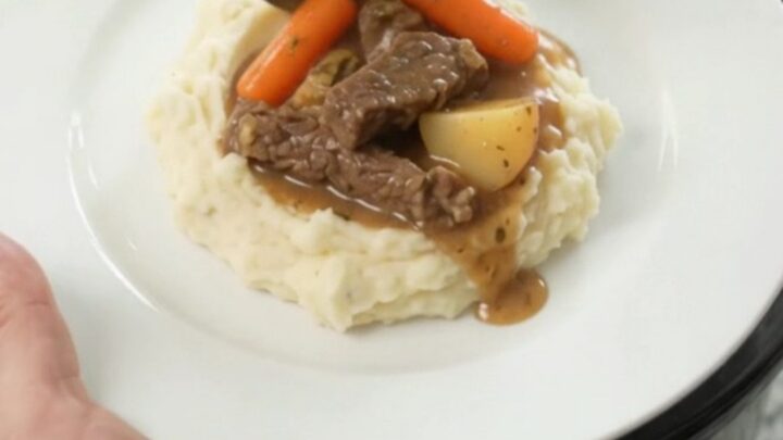 Slow cooker filled with tender flank steak, baby carrots, and red potatoes in a golden butter au jus.