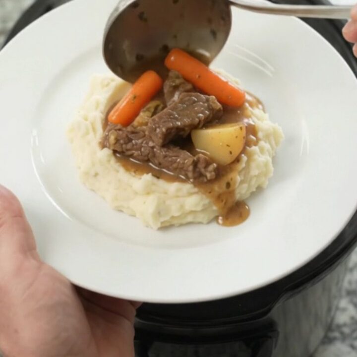 Slow cooker filled with tender flank steak, baby carrots, and red potatoes in a golden butter au jus.