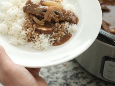 Slow cooker flank steak with portobello mushrooms and bourbon gravy, bubbling in a black Crockpot.