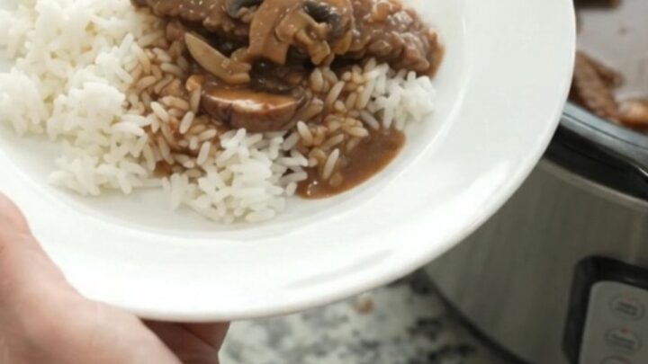 Slow cooker flank steak with portobello mushrooms and bourbon gravy, bubbling in a black Crockpot.