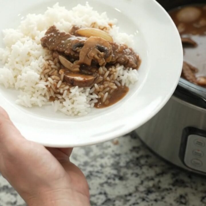 Slow cooker flank steak with portobello mushrooms and bourbon gravy, bubbling in a black Crockpot.
