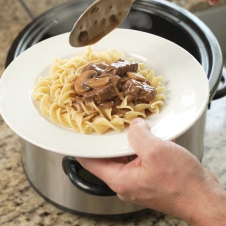 Slow cooker full of braised flank steak, portobello mushrooms, and shallots in a rich sour cream gravy.