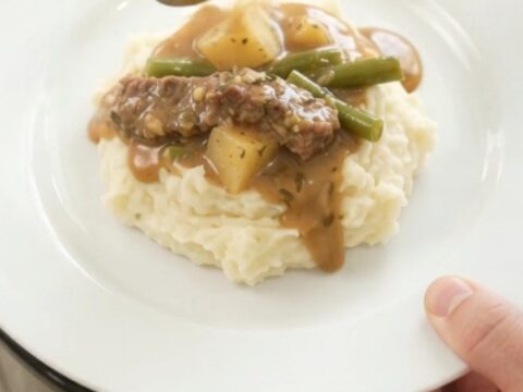 Slow cooker filled with tender flank steak, green beans, and potatoes in a golden butter au jus