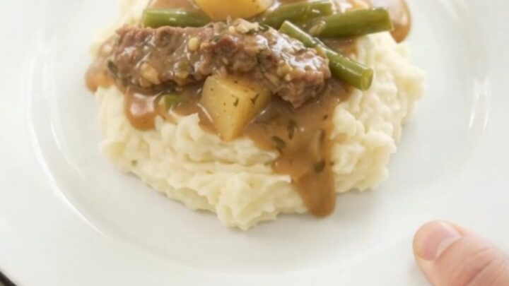 Slow cooker filled with tender flank steak, green beans, and potatoes in a golden butter au jus