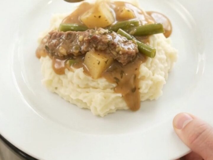 Slow cooker filled with tender flank steak, green beans, and potatoes in a golden butter au jus