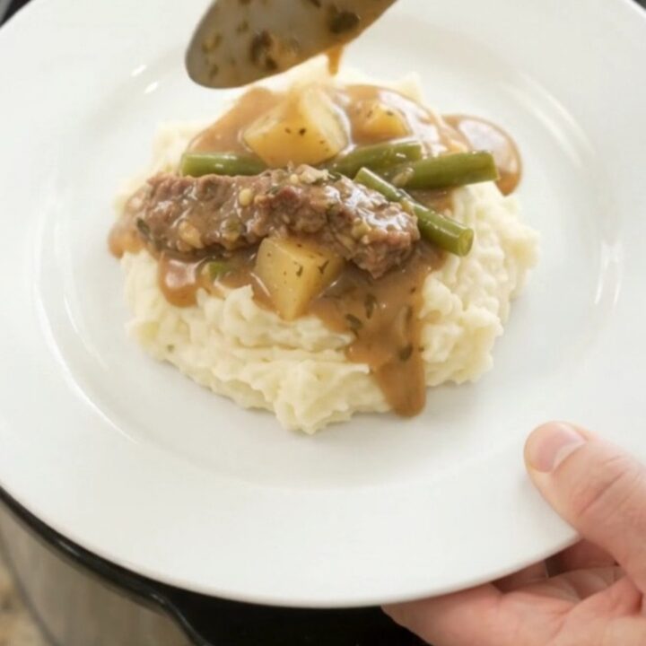 Slow cooker filled with tender flank steak, green beans, and potatoes in a golden butter au jus