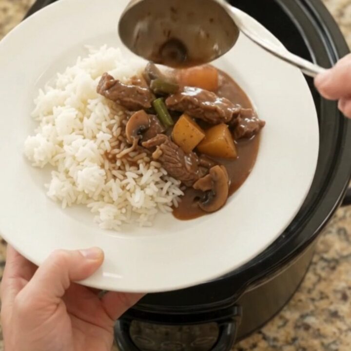 Slow cooker bourbon gravy flank steak with green beans and potatoes, bubbling in the crockpot.