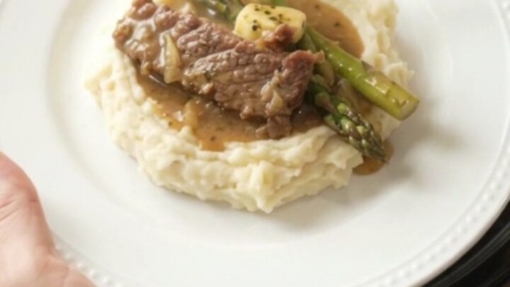 Slow cooker filled with tender flank steak and asparagus in a golden garlic butter au jus.