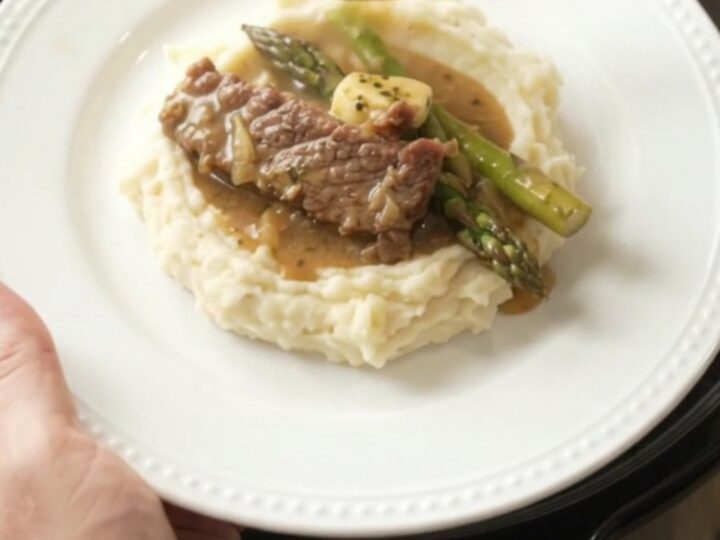 Slow cooker filled with tender flank steak and asparagus in a golden garlic butter au jus.