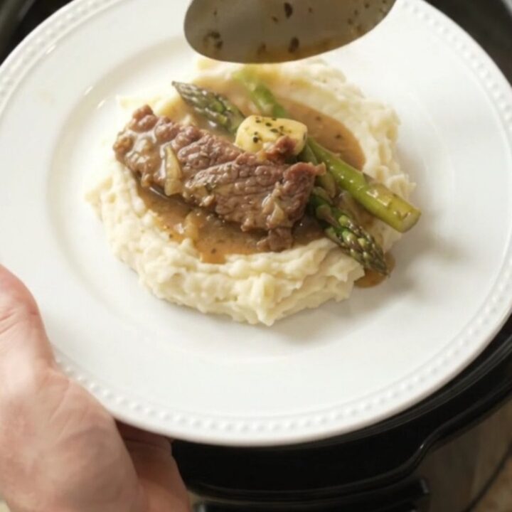 Slow cooker filled with tender flank steak and asparagus in a golden garlic butter au jus.