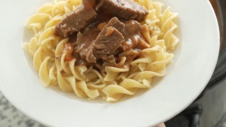 Slow cooker full of creamy stroganoff with flank steak, pearl onions, and carrots