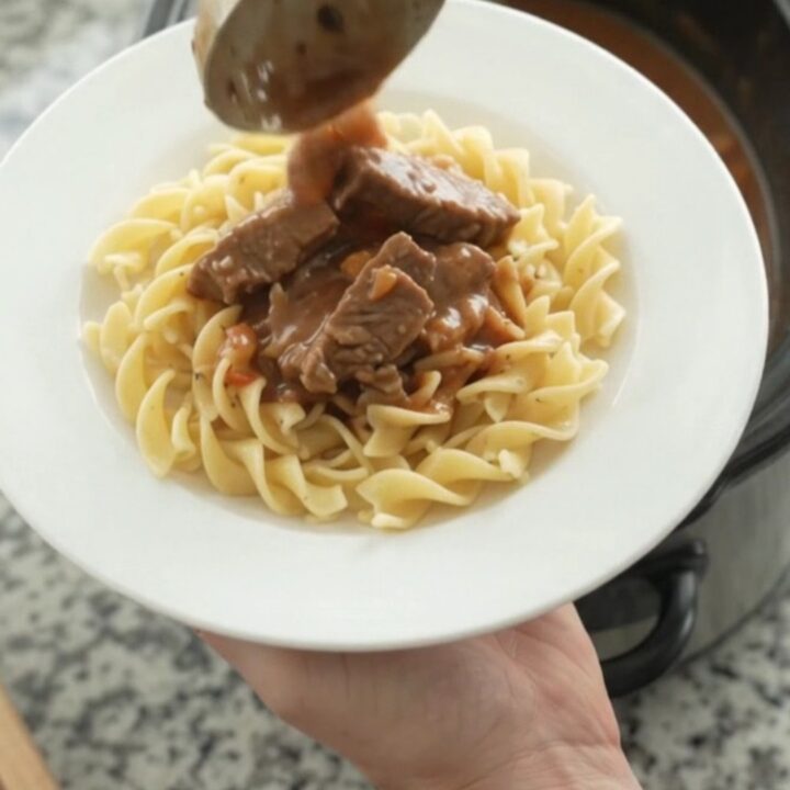 Slow cooker full of creamy stroganoff with flank steak, pearl onions, and carrots