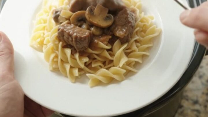 Beef tenderloin tips in creamy mushroom gravy served over buttered egg noodles in a white bowl.