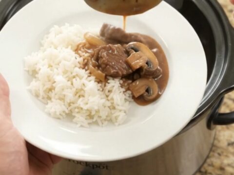 Slow cooker beef tenderloin tips in bourbon mushroom gravy, served over white rice on a white porcelain plate.
