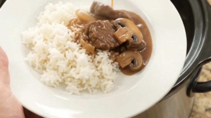 Slow cooker beef tenderloin tips in bourbon mushroom gravy, served over white rice on a white porcelain plate.
