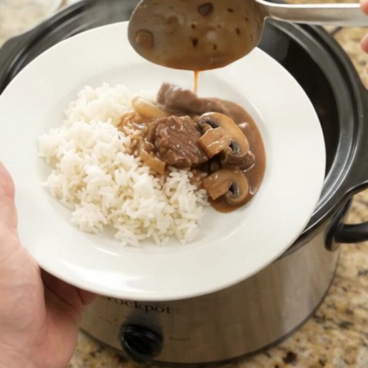 Slow cooker beef tenderloin tips in bourbon mushroom gravy, served over white rice on a white porcelain plate.