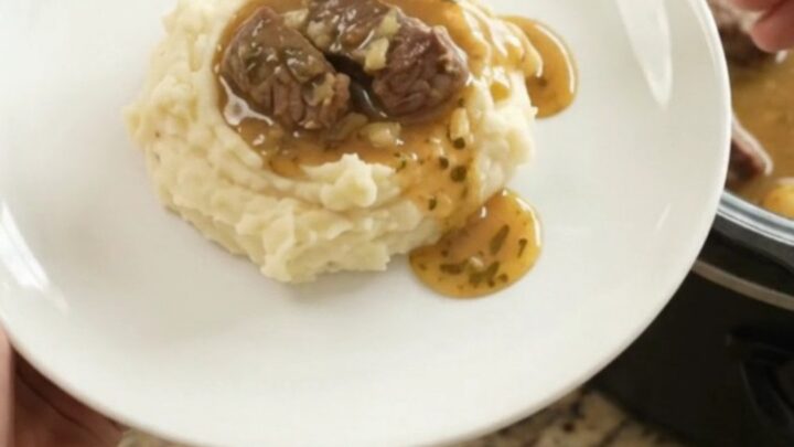 Slow cooker full of tender beef tips and golden potatoes in a buttery au jus
