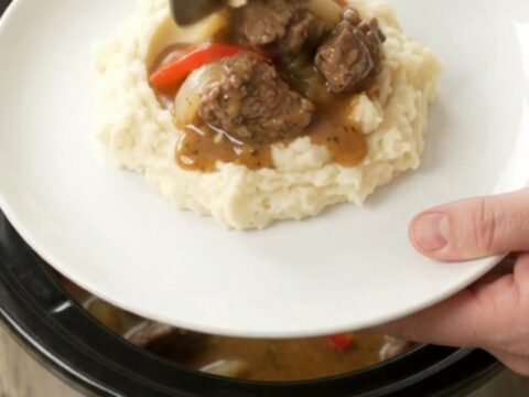 Slow-cooker beef tenderloin tips with peppers and onions in a rich golden sauce, served in a black ceramic crockpot