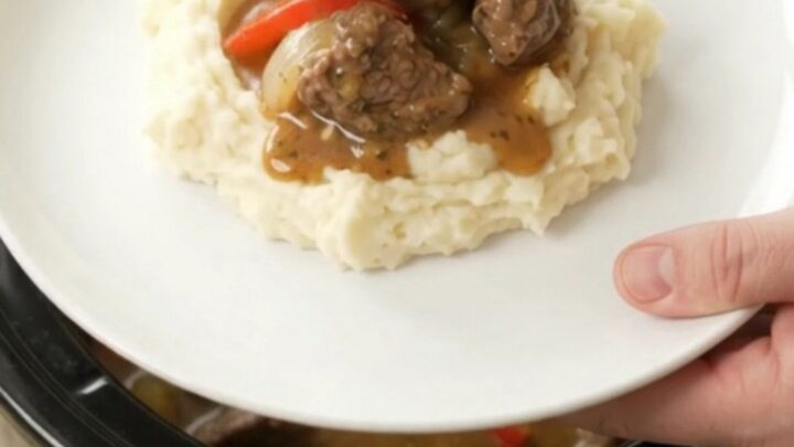 Slow-cooker beef tenderloin tips with peppers and onions in a rich golden sauce, served in a black ceramic crockpot
