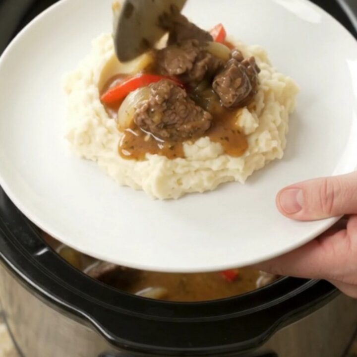 Slow-cooker beef tenderloin tips with peppers and onions in a rich golden sauce, served in a black ceramic crockpot
