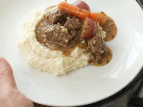 Slow cooker full of beef tenderloin tips, carrots, and potatoes in a rich butter au jus