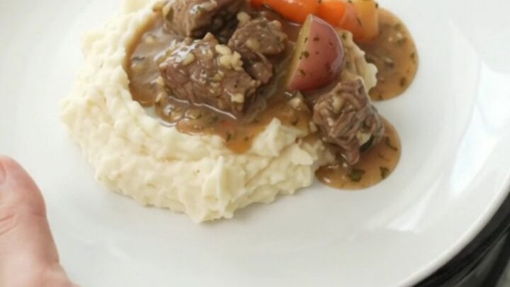 Slow cooker full of beef tenderloin tips, carrots, and potatoes in a rich butter au jus