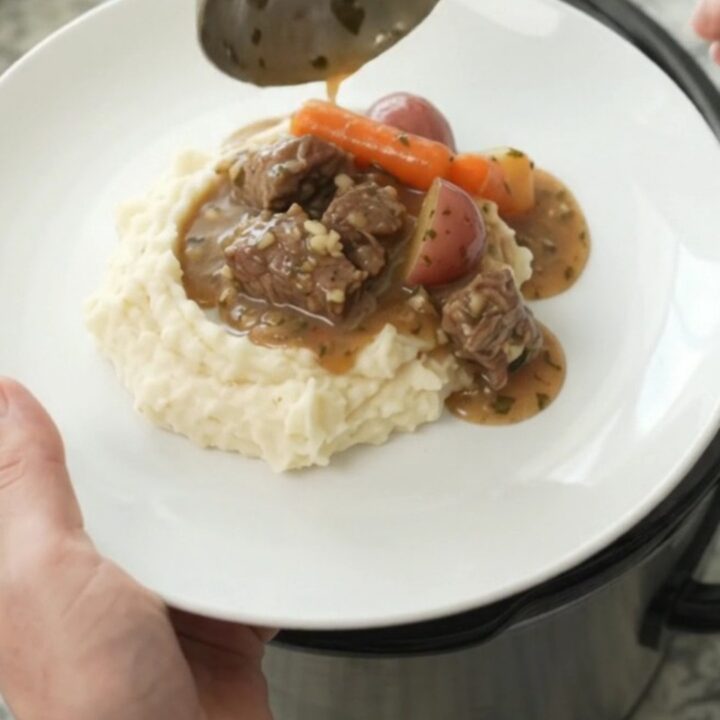 Slow cooker full of beef tenderloin tips, carrots, and potatoes in a rich butter au jus