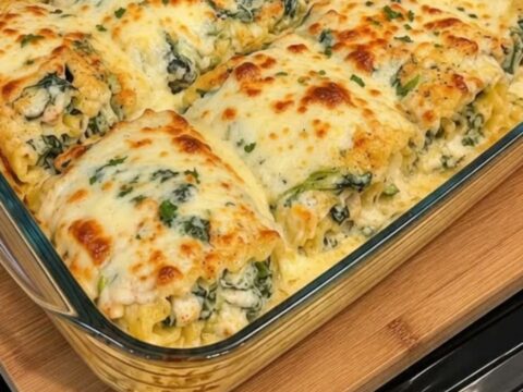 A close-up of a chicken Alfredo lasagna roll-up being lifted with a spatula, showing a gooey cheese pull.