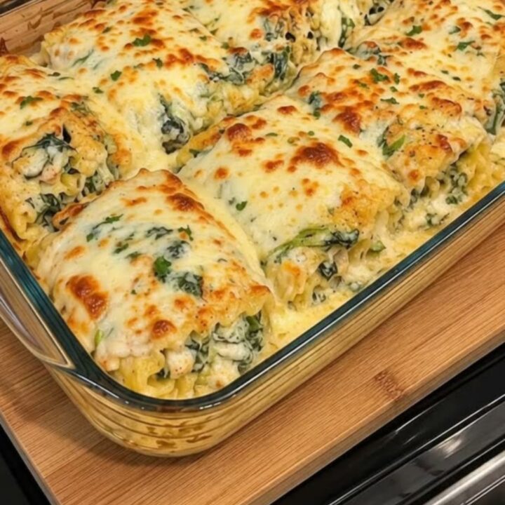 A close-up of a chicken Alfredo lasagna roll-up being lifted with a spatula, showing a gooey cheese pull.