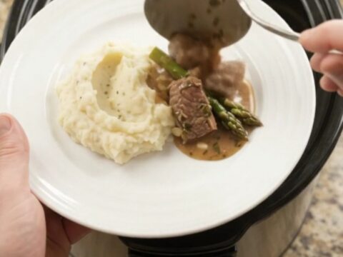 Slow cooker filled with beef tenderloin tips and asparagus in a buttery au jus