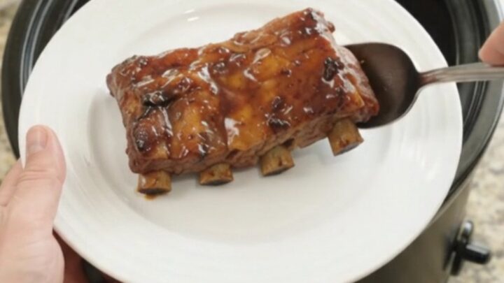 Slow-cooker baby back ribs with apples and molasses glaze, garnished with fresh herbs.