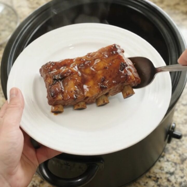 Slow-cooker baby back ribs with apples and molasses glaze, garnished with fresh herbs.