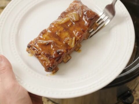 Tender baby back ribs glazed with maple bourbon BBQ sauce in a slow cooker, garnished with onions.