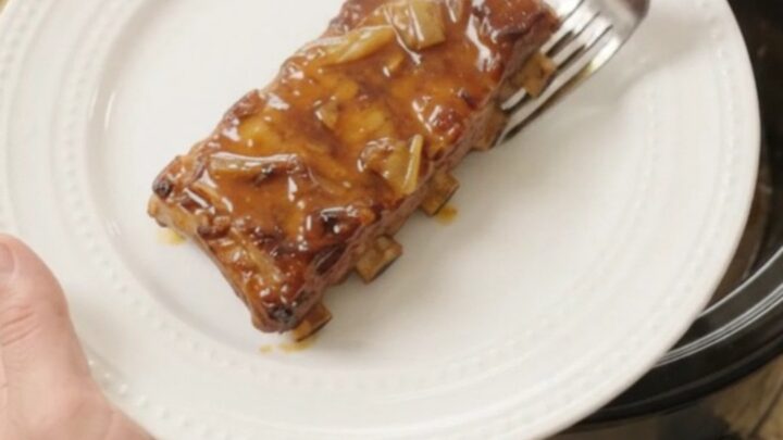Tender baby back ribs glazed with maple bourbon BBQ sauce in a slow cooker, garnished with onions.
