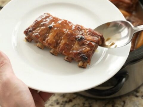 Slow-cooker baby back ribs with caramelized apples and honey hickory glaze in a black ceramic crockpot.