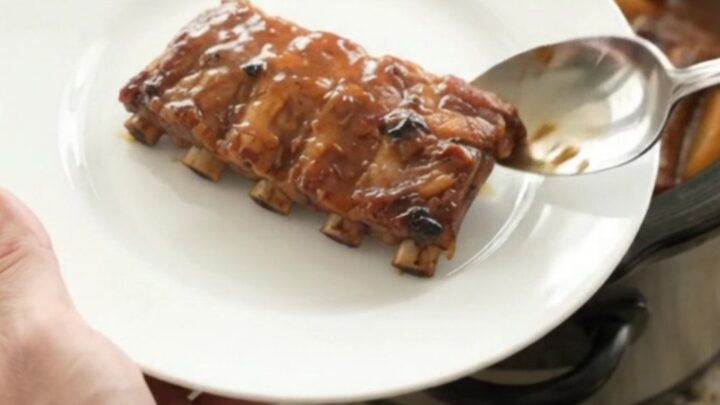 Slow-cooker baby back ribs with caramelized apples and honey hickory glaze in a black ceramic crockpot.