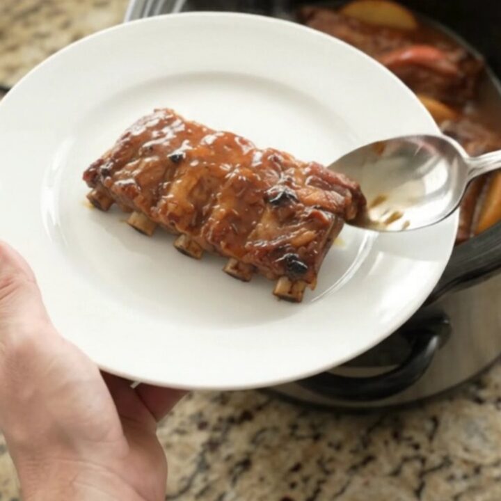 Slow-cooker baby back ribs with caramelized apples and honey hickory glaze in a black ceramic crockpot.