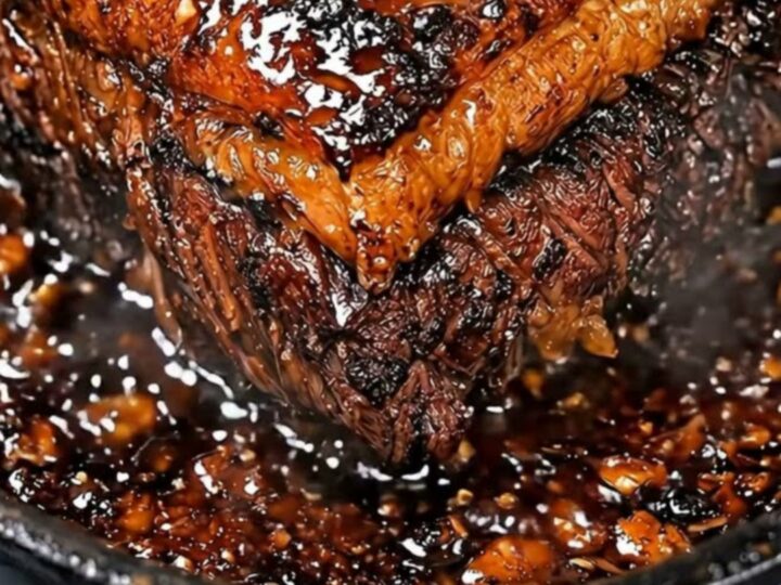 A close-up view of a sticky, glossy honey garlic glazed pot roast resting in a seasoned cast iron skillet.