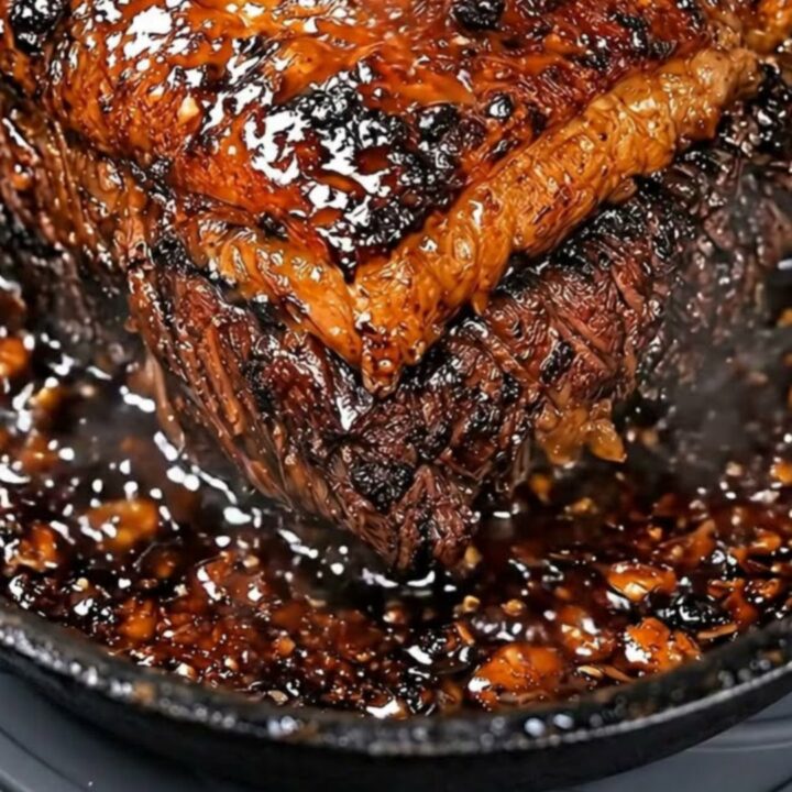 A close-up view of a sticky, glossy honey garlic glazed pot roast resting in a seasoned cast iron skillet.