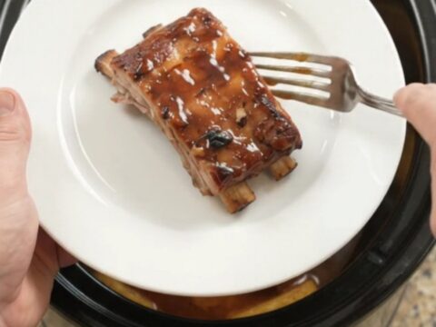 Slow cooker baby back ribs with pineapple rings and BBQ sauce, glistening in the crockpot.