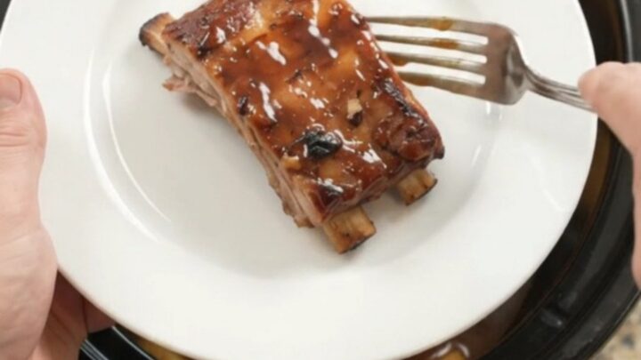 Slow cooker baby back ribs with pineapple rings and BBQ sauce, glistening in the crockpot.