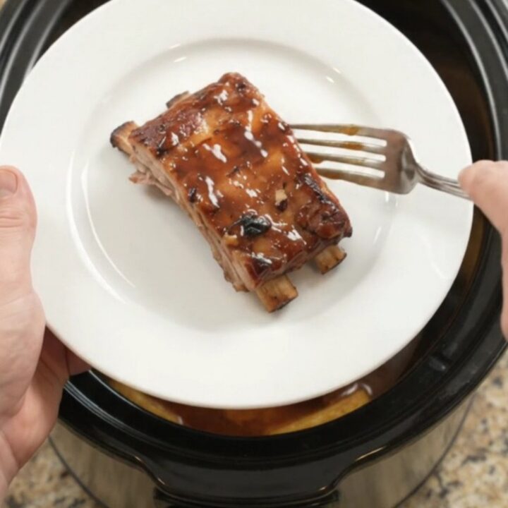 Slow cooker baby back ribs with pineapple rings and BBQ sauce, glistening in the crockpot.