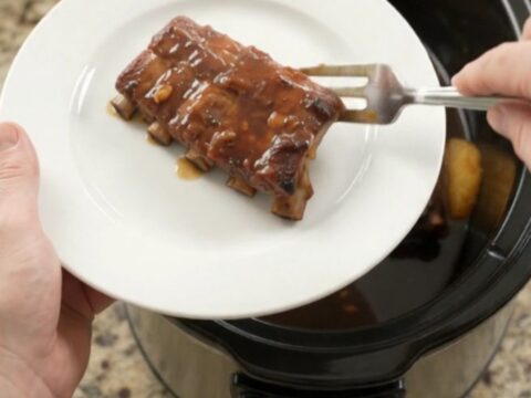 Slow-cooker baby back ribs with pineapple rings and molasses garlic glaze, bubbling in a black crockpot.