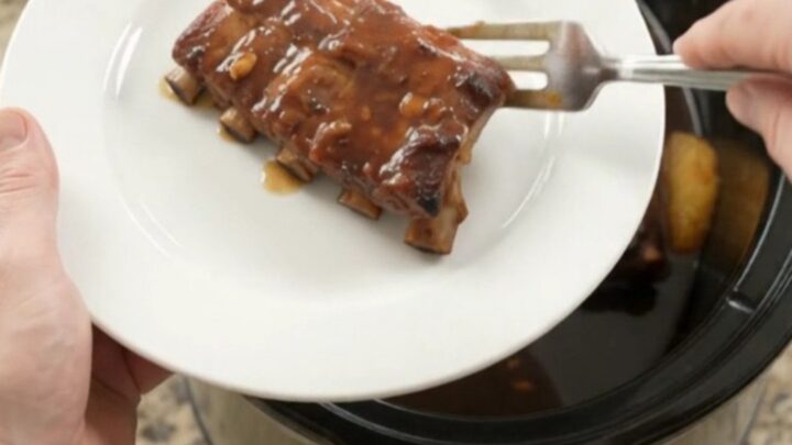 Slow-cooker baby back ribs with pineapple rings and molasses garlic glaze, bubbling in a black crockpot.