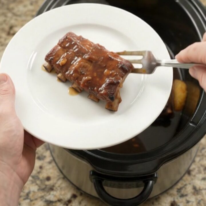 Slow-cooker baby back ribs with pineapple rings and molasses garlic glaze, bubbling in a black crockpot.