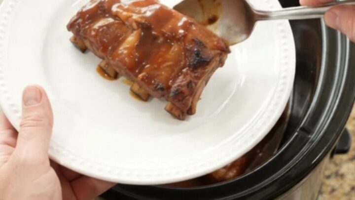 Slow-cooker pineapple BBQ baby back ribs in a black crockpot with pineapple rings and sauce