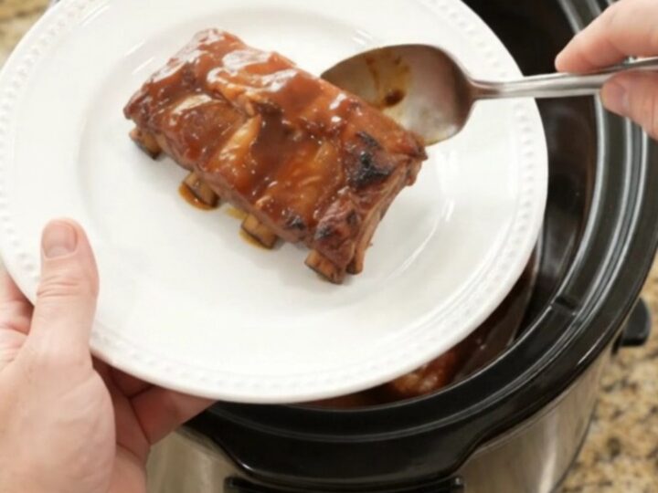 Slow-cooker pineapple BBQ baby back ribs in a black crockpot with pineapple rings and sauce